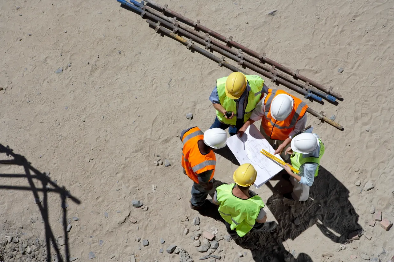 Four construction workers reviewing plans at a site.