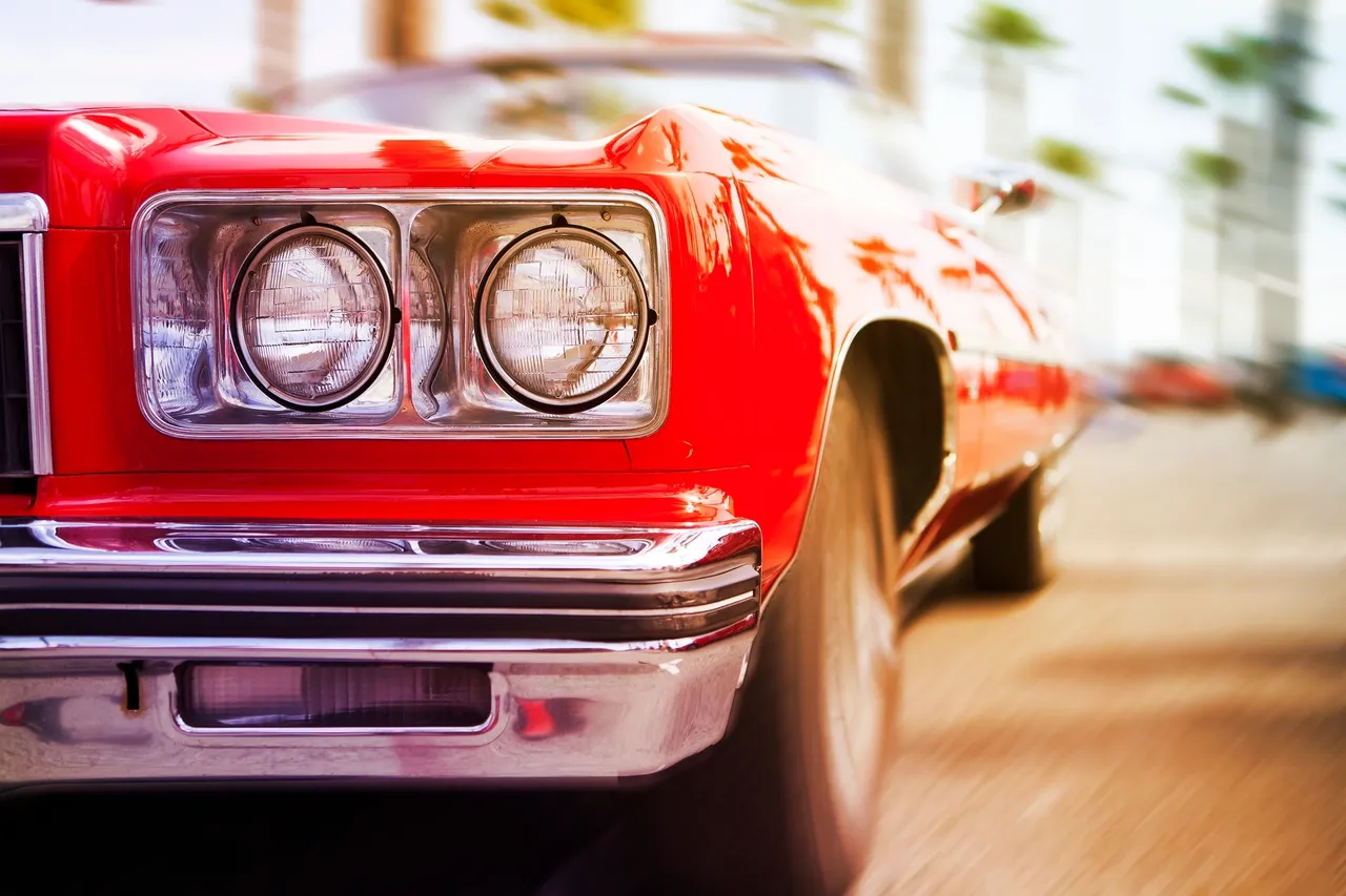 Close-up of the front left headlight and wheel of a red classic car.
