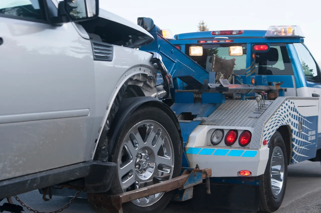 A damaged white car being towed by a blue tow truck.