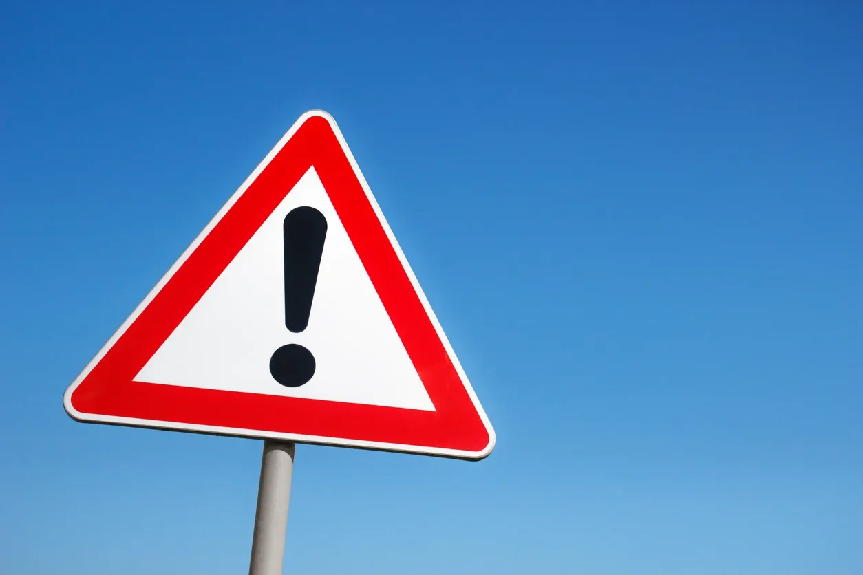 A triangular warning sign with an exclamation mark against a clear blue sky.