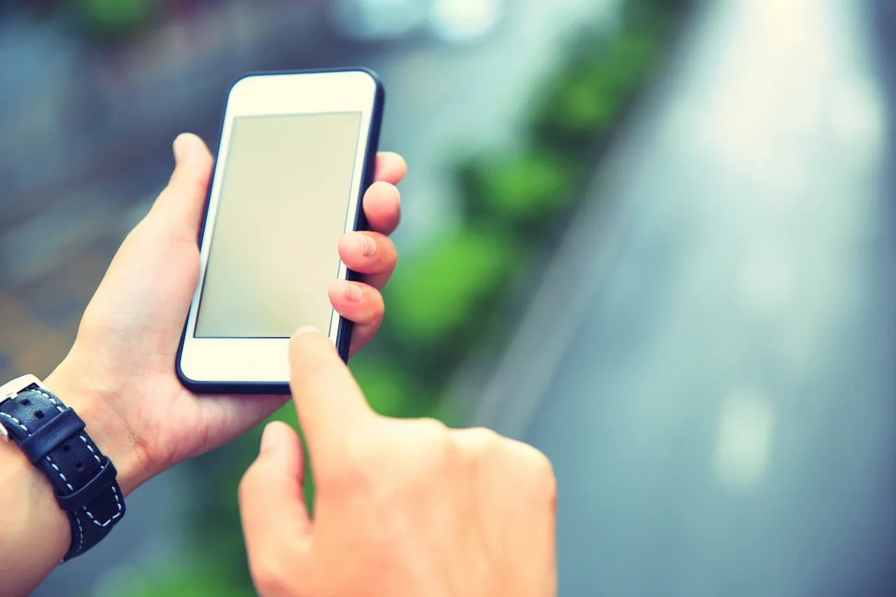 A person holding and using a smartphone with a blank screen.