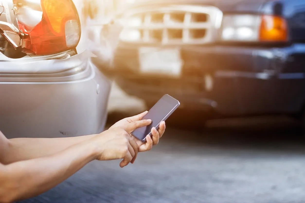 Person using a smartphone near a parked car's headlight.