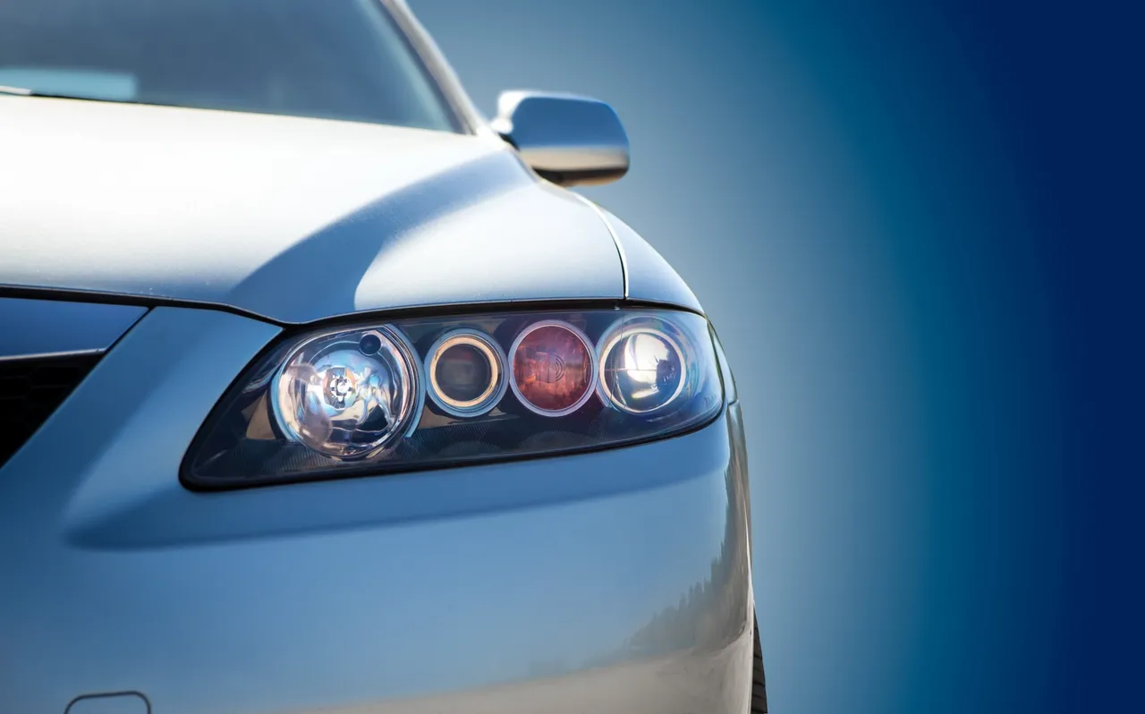 Close-up of a sleek silver car's headlight under a clear blue sky.