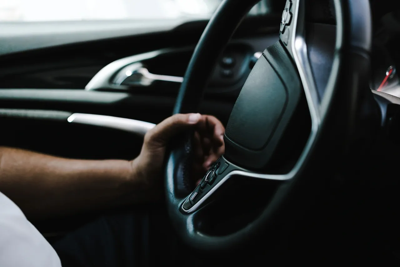 A person gripping a car steering wheel with a modern interior.