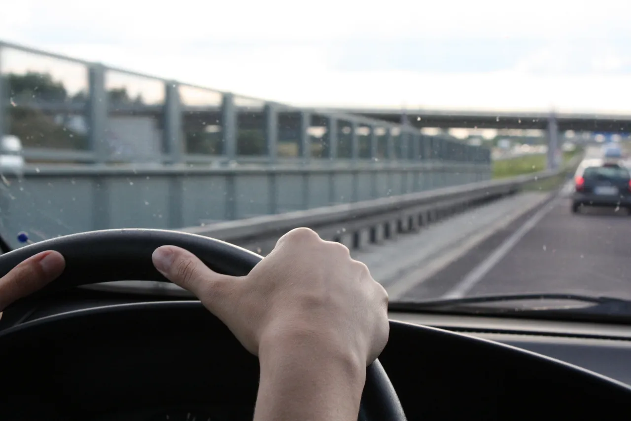A hand on a car steering wheel driving on a highway.