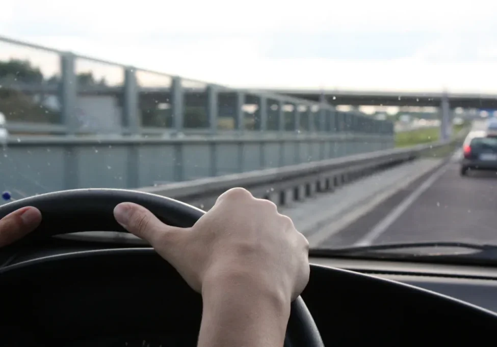 A hand on a car steering wheel driving on a highway.