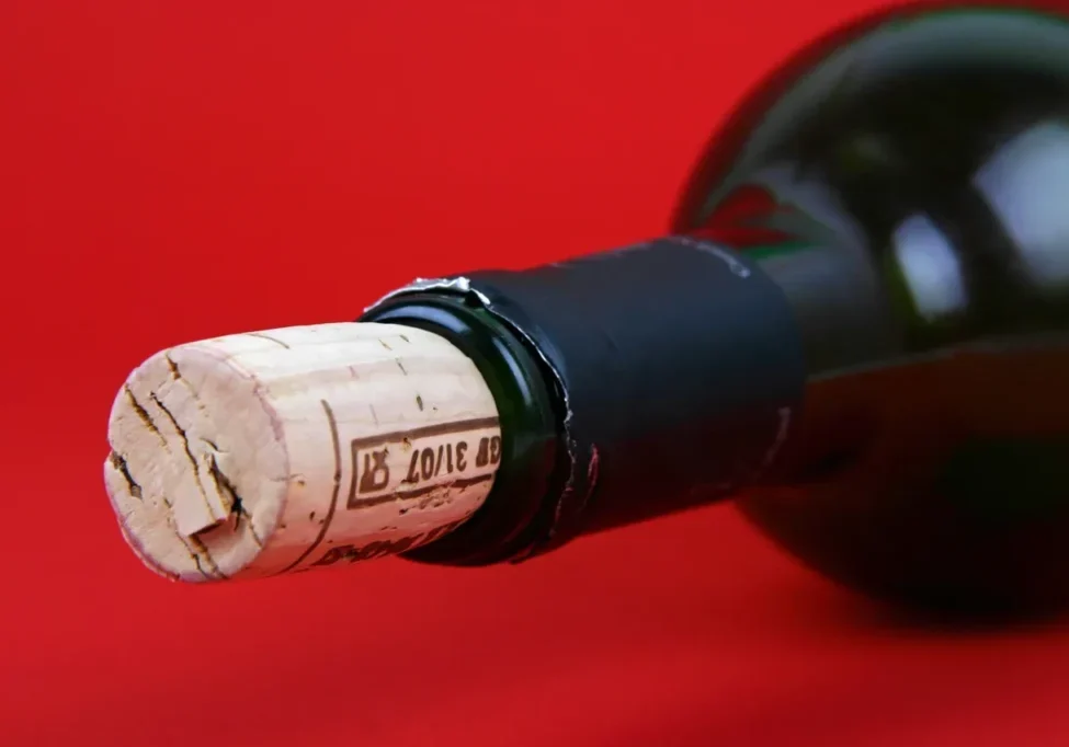 Close-up of a wine bottle with cork partially inserted on a red background.
