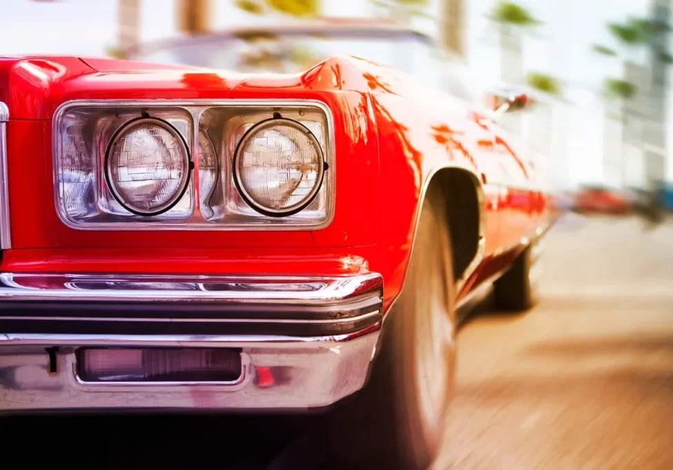 Close-up of the front left headlight and wheel of a red classic car.