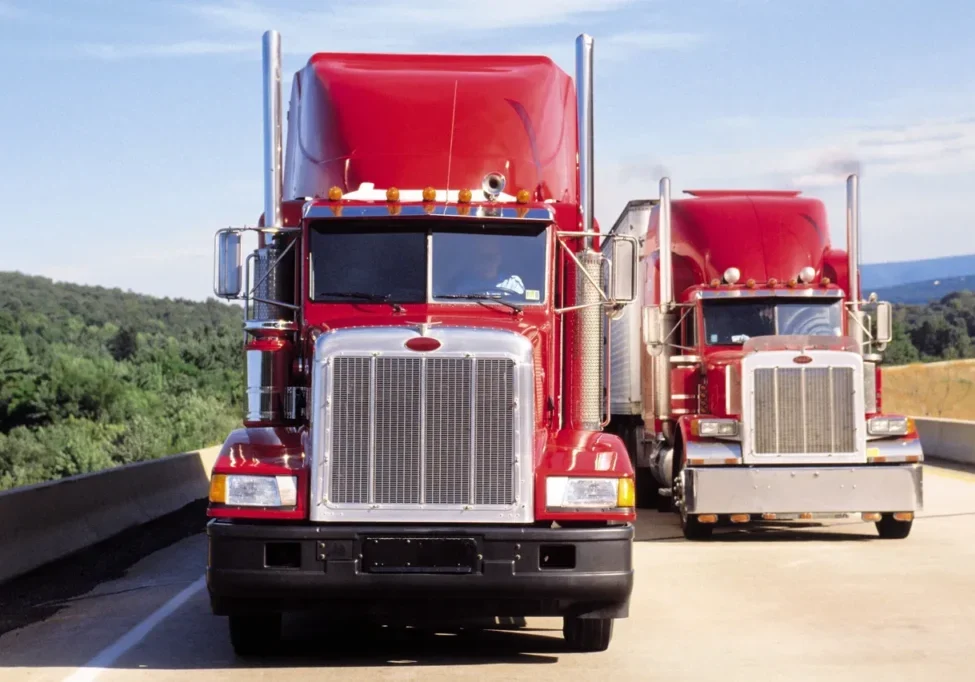 Two red semi-trucks driving on a highway.