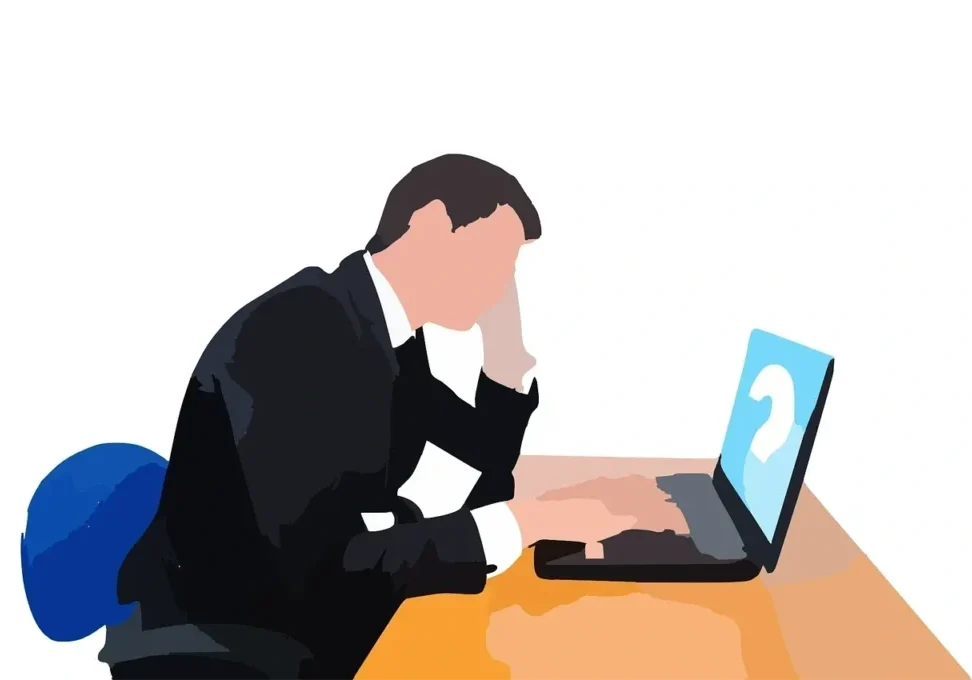 A stressed man in a suit working on a laptop.