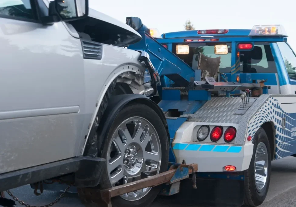 A damaged white car being towed by a blue tow truck.