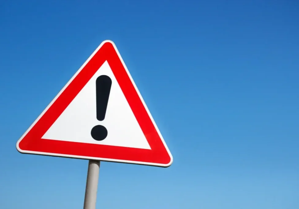 A triangular warning sign with an exclamation mark against a clear blue sky.