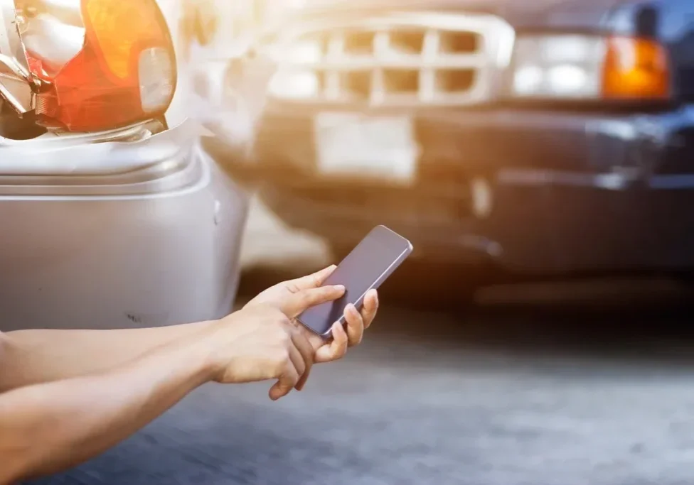 Person using a smartphone near a parked car's headlight.