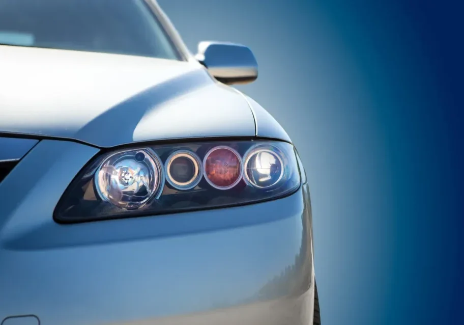 Close-up of a sleek silver car's headlight under a clear blue sky.