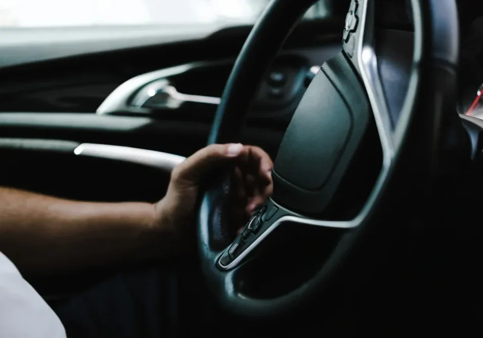 A person gripping a car steering wheel with a modern interior.